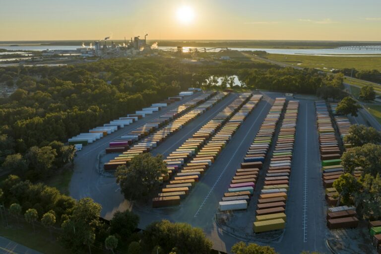 Aerial view of large cargo container yard with rows of freight containers and big factory